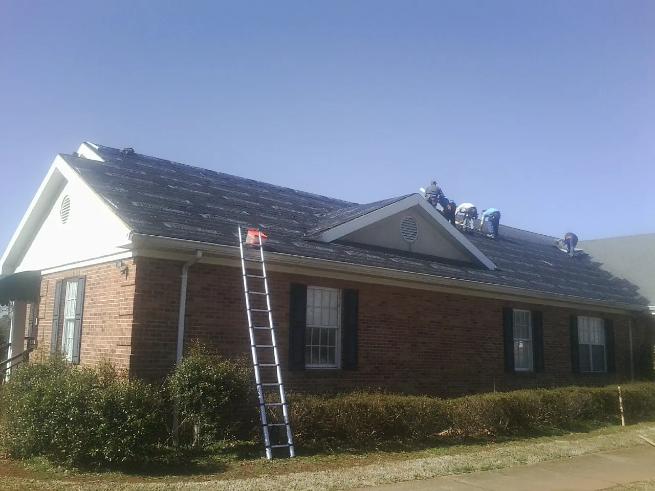 Crew tearing shingles off a brick ranch roof with a ladder set — Emergency Roof Repair work by our crew in Cortland