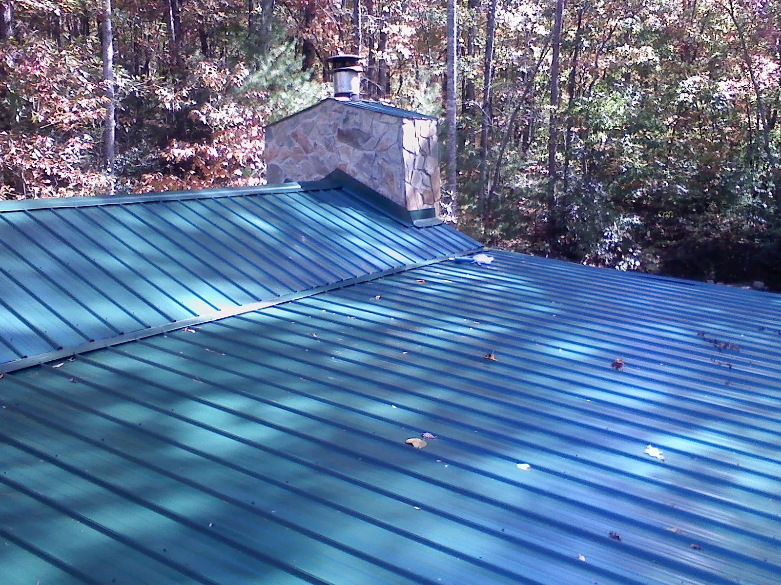 New green metal roof and stone chimney surrounded by autumn woods in Cortland
